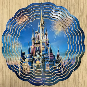 May include: A metal wind spinner featuring a colorful image of Cinderella's Castle with fireworks in the background. The spinner has multiple layers of metal that spin in the wind.