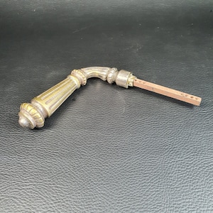 Puede incluir: Una manija de puerta de latón vintage con un diseño decorativo y una varilla de metal.