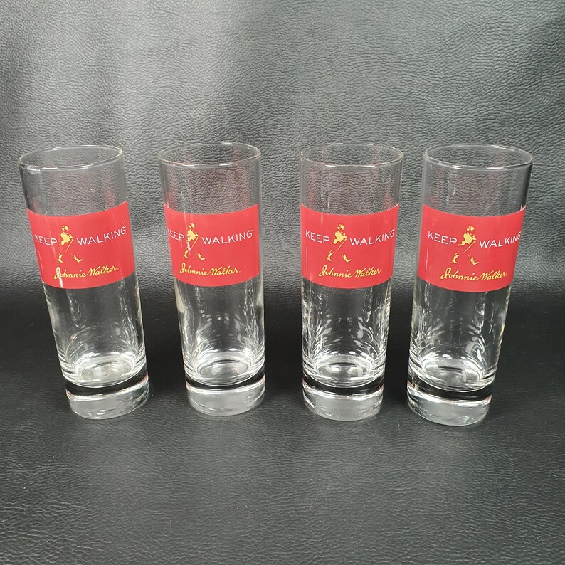 May include: Four clear glass shot glasses with a red label that says "Keep Walking Johnnie Walker".