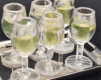 May include: Six clear glass shot glasses filled with a light green liquid, sitting on a silver tray.