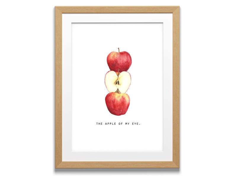 May include: A framed print featuring a watercolor illustration of three red apples stacked vertically. The middle apple is sliced in half, revealing the interior. The text "THE APPLE OF MY EYE." is below the apples.