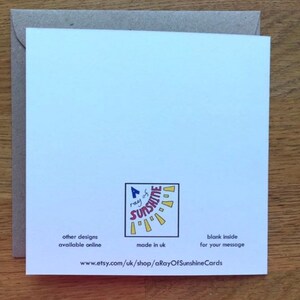 May include: A white card with a colorful sun graphic and the text "a ray of sunshine" in red and blue. The card has the text "other designs available online" and "made in uk" on the bottom left and "blank inside for your message" on the bottom right. The text "www.etsy.com/uk/shop/aRayOfSunshineCards" is printed on the bottom center.