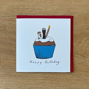 May include: A birthday card featuring a cupcake illustration with candles and beer glasses. The cupcake has a blue liner, brown cake, and white frosting. The card has a red border and the words "Happy Birthday" are written in black.