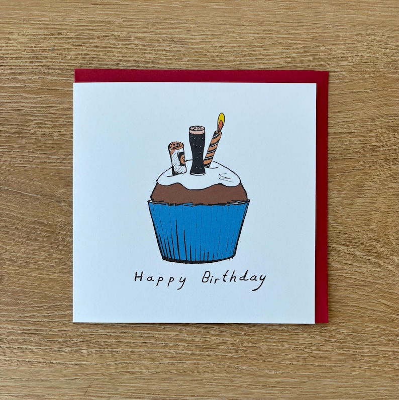 May include: A birthday card featuring a cupcake illustration with candles and beer glasses. The cupcake has a blue liner, brown cake, and white frosting. The card has a red border and the words "Happy Birthday" are written in black.