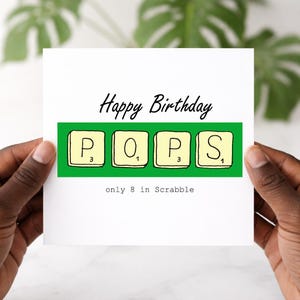 May include: A white ceramic mug with a black handle and the text "But First, Coffee" in a bold, black font. The mug is set against a blurred background, suggesting a cosy setting.