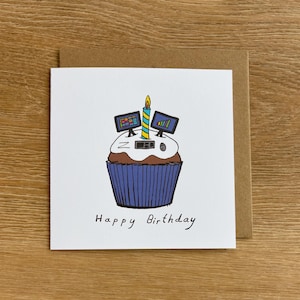 May include: A white greeting card with a brown envelope. The card features a cupcake illustration with computer monitor decorations, a candle, and the words "Happy Birthday". The cupcake has a blue liner.