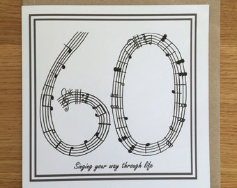 Op de afbeelding: Een witte kaart met een grijze rand. Het getal 60 wordt gevormd met behulp van muzieknoten. De tekst "Singing your way through life" staat onder het getal.