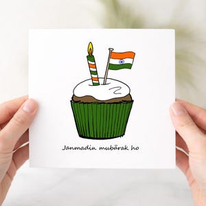 May include: A greeting card featuring a cupcake with white frosting, a green wrapper, and a candle with orange and green stripes. An Indian flag is also on the cupcake. The text "Janmadin mubārak ho" is at the bottom.