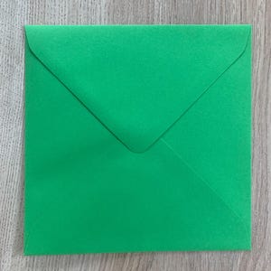 Op de afbeelding: Een vierkante, heldergroene envelop met een driehoekige flap. De papieren envelop ligt op een lichtbruin houten oppervlak. De envelop is gesloten en klaar om te worden verzegeld.
