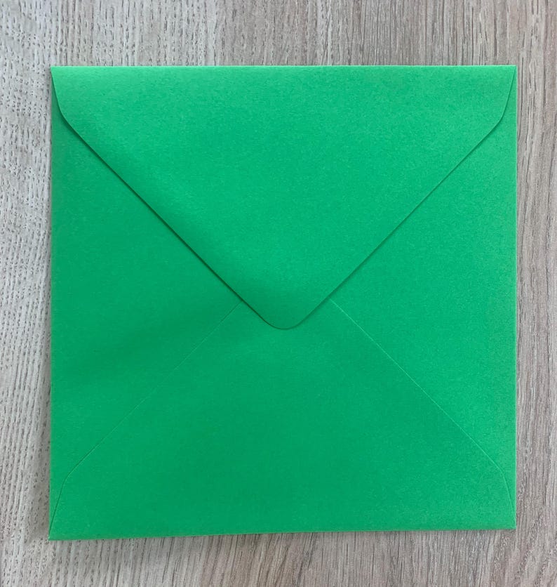 Op de afbeelding: Een vierkante, heldergroene envelop met een driehoekige flap. De papieren envelop ligt op een lichtbruin houten oppervlak. De envelop is gesloten en klaar om te worden verzegeld.