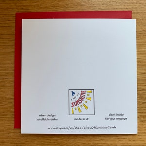 May include: A white card with a red border. The card has a yellow sun with rays and the text "A ray of sunshine" in blue and red. The text "other designs available online" is in black. The text "made in uk" is in black. The text "blank inside for your message" is in black. The text "www.etsy.com/uk/shop/aRayOfSunshineCards" is in black.