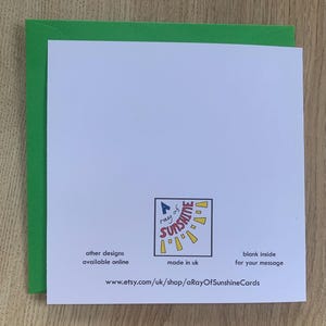 Op de afbeelding: Een witte wenskaart met een groene rand, met een logo met de tekst "A ray of sunshine". De kaart bevat de tekst "other designs available online", "made in uk" en "blank inside for your message". De Etsy shop URL is ook zichtbaar.