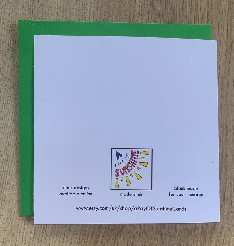 Op de afbeelding: Een witte wenskaart met een groene rand, met een logo met de tekst "A ray of sunshine". De kaart bevat de tekst "other designs available online", "made in uk" en "blank inside for your message". De Etsy shop URL is ook zichtbaar.