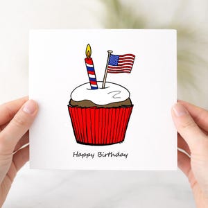 May include: A white birthday card with a cupcake illustration. The cupcake has a red wrapper, chocolate base, and white frosting, topped with a lit candle and an American flag. The words "Happy Birthday" are written below.