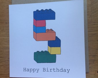 May include: A square greeting card with a white background featuring a large number five constructed from colorful plastic building blocks in shades of blue, red, orange, yellow, and green. The text Happy Birthday is printed in black below.