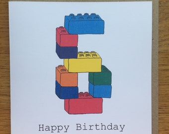 May include: A square greeting card featuring a graphic of the number six constructed from colorful interlocking plastic building bricks in blue, red, yellow, orange, and green. The text Happy Birthday is printed in black below the number.