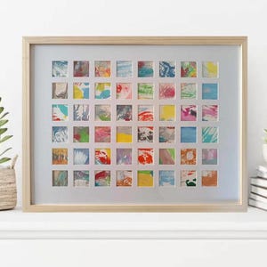 Può includere: Un'opera d'arte incorniciata che presenta una griglia di 49 quadrati colorati, ognuno con un design astratto unico. I quadrati sono disposti in una griglia e sono incorniciati in una cornice di legno chiaro.