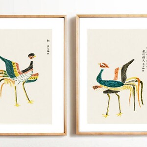 Puede incluir: Dos impresiones enmarcadas de ilustraciones estilizadas de pájaros con largas colas de colores. Las impresiones están sobre un fondo blanco y presentan texto japonés.