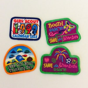 Op de afbeelding: Vier Girl Scout-badges met kleurrijke borduurwerk. De badges tonen de tekst "Girl Scout", "1999 Calendar Sale", "Booth Cookies '99", "Share the Adventure" en "1999 Girl Scout Thinking Day".