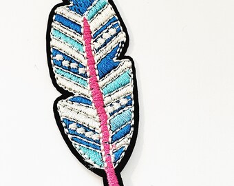 Könnte beinhalten: Eine blaue und weiße gestickte Feder mit einem rosa Stiel. Die Feder hat ein geometrisches Muster.