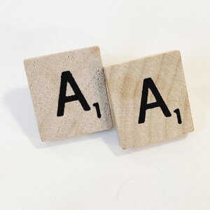 Puede incluir: Dos fichas de Scrabble de madera con la letra "A" en cada una. Cada ficha tiene un valor de 1 punto.