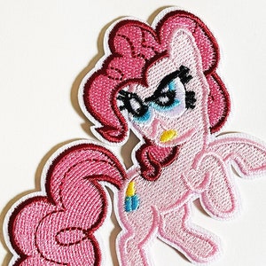 Puede incluir: Pinkie Pie de My Little Pony lleva gafas y tiene una expresión seria. El parche bordado es rosa y blanco.