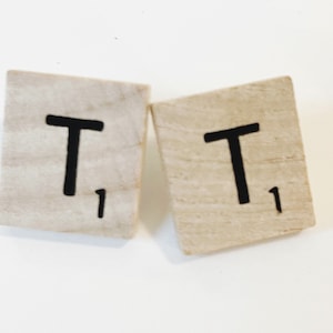 Puede incluir: Dos fichas de letras de madera con la letra "T" impresa en ellas. Cada ficha tiene un valor de "1" impreso en ella.