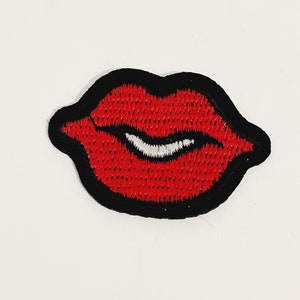 Könnte beinhalten: Roter Lippen-Stickerei-Aufnäher mit schwarzem Umriss. Die Lippen sind leicht geöffnet und zeigen ein weißes Lächeln.