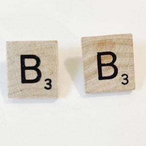 May include: Two wooden letter tiles with the letter "B" and the number "3" printed on them. The tiles are light brown and the letter is black.