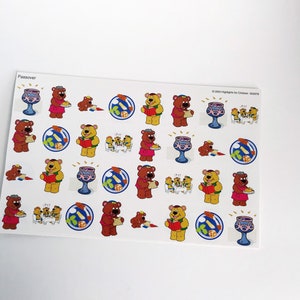 May include: A sheet of stickers featuring a variety of Passover-themed images. The stickers feature bears wearing yarmulkes, holding matzah, and celebrating Passover. The stickers are on a white background and have a blue and white border.