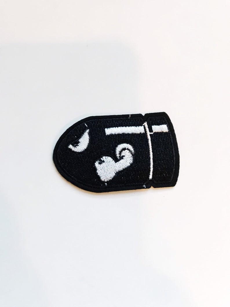 Puede incluir: Parche bordado negro con forma de bala con detalles blancos. El parche presenta una luna creciente blanca y un coraz&oacute;n blanco.