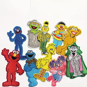 Könnte beinhalten: Eine Sammlung von zehn gestickten Stoffaufnähern mit farbenfrohen Sesame Street-Figuren, darunter Elmo, Cookie Monster, Big Bird, Oscar the Grouch, Bert, Ernie, Zoe, Abby Cadabby, Grover und Count von Count auf einem weißen Hintergrund.