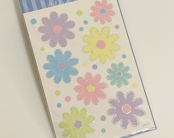 Può includere: Due fogli di adesivi di fiori color pastello con dettagli glitterati. Gli adesivi sono su uno sfondo bianco con un bordo a strisce blu e bianco. Il testo "Added Touch" è stampato sulla confezione.