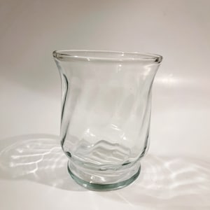 Peut inclure: Un vase en verre transparent avec un motif texturé et ondulé. Le vase a une large ouverture et une base arrondie.