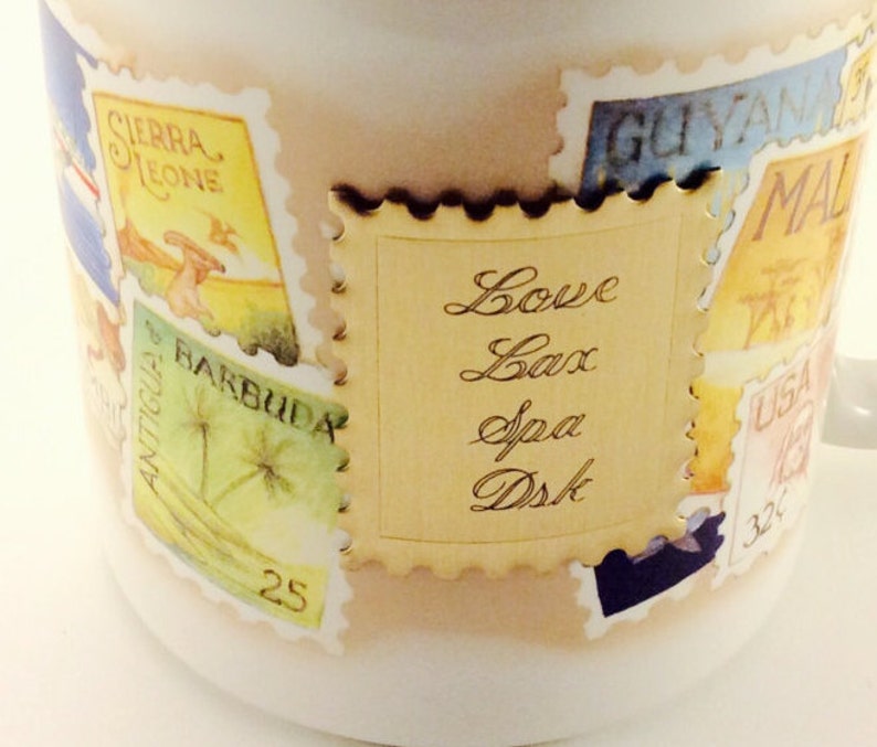 May include: A white ceramic mug with a gold-colored stamp design. The stamp features a gold background with the text "Love Lax Spa Dsk" written in cursive.