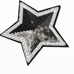 May include: A black star-shaped patch with a silver sequin design. The star has a white border.