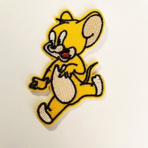 May include: Embroidered patch featuring a yellow cartoon mouse in a running pose. The mouse has a beige belly and ears, a red mouth, and black outlines. The patch is likely for clothing or accessories.