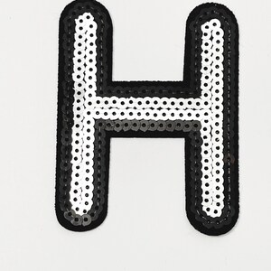Peut inclure: Un écusson de lettre "H" en paillettes noires et blanches. La lettre est bordée de noir et remplie de rangées de paillettes blanches et noires. Ce patch peut servir à décorer des vêtements ou des sacs.