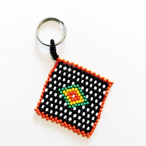 May include: A black and white beaded keyring with a colourful beaded design in the centre. The keyring is attached to a silver ring.