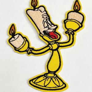 Può includere: Toppa ricamata gialla da stirare con un candelabro di cartone animato con una faccia e la lingua che sporge. Il candelabro ha tre braccia, ciascuna con una candela gialla con una fiamma rossa.