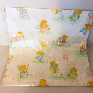 May include: A sheet of wrapping paper with a light yellow background and a repeating pattern of teddy bears wearing different colored clothes and holding balloons, presents, and other party favors.