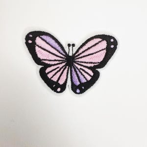 May include: Embroidered butterfly patch with a white border. The butterfly features a design with pink and purple wings outlined in black. The patch is a decorative item, suitable for clothing or accessories.
