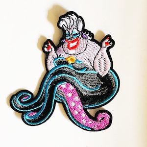 May include: An embroidered iron-on patch featuring Ursula, the sea witch from Disney's The Little Mermaid. Ursula is depicted with her signature purple skin, long white hair, and a mischievous grin. She is sitting on her octopus tentacles, which are a mix of black, blue, and pink.