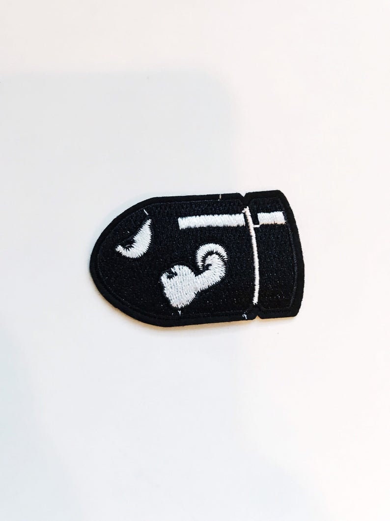 Puede incluir: Parche bordado negro con forma de bala con detalles blancos. El parche presenta una luna creciente blanca y un coraz&oacute;n blanco.