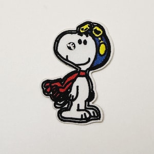 May include: Embroidered patch featuring Snoopy as a World War I flying ace. The patch shows Snoopy in a white body with a red scarf, blue and yellow goggles, and a black outline. A fun, colorful patch for clothing or accessories.