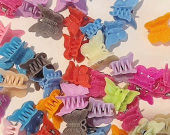 May include: A collection of colorful butterfly hair clips in various shades of blue, pink, purple, orange, yellow, and brown. The clips are made of plastic and have a textured surface.