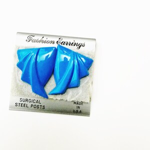 May include: Bright blue fashion earrings with a folded design. The earrings are on a card that reads "Fashion Earrings" and "Surgical Steel Posts." The card also states "Made in U.S.A."