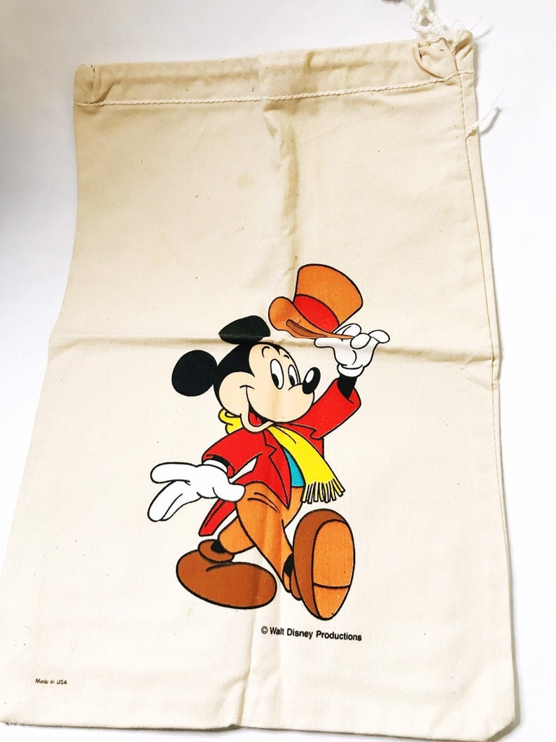 Może przedstawiać: Beżowa torba ze sznurkiem ze kolorową grafiką Myszki Miki w czerwonej kurtce, brązowych spodniach i ż&oacute;łtym szaliku. Miki trzyma pomarańczowy kapelusz. Torba ma napis "Walt Disney Productions".