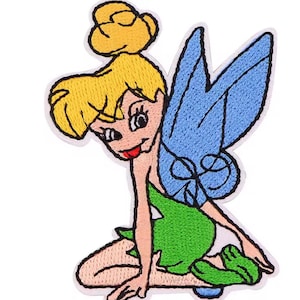 May include: Embroidered patch featuring a cartoon fairy with blonde hair, blue wings, and a green dress. The fairy is kneeling with a playful expression, outlined in white.