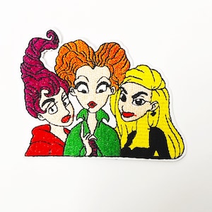 May include: Embroidered patch featuring three cartoon witches with red, green, and black outfits. The witches have red, orange, and yellow hair.